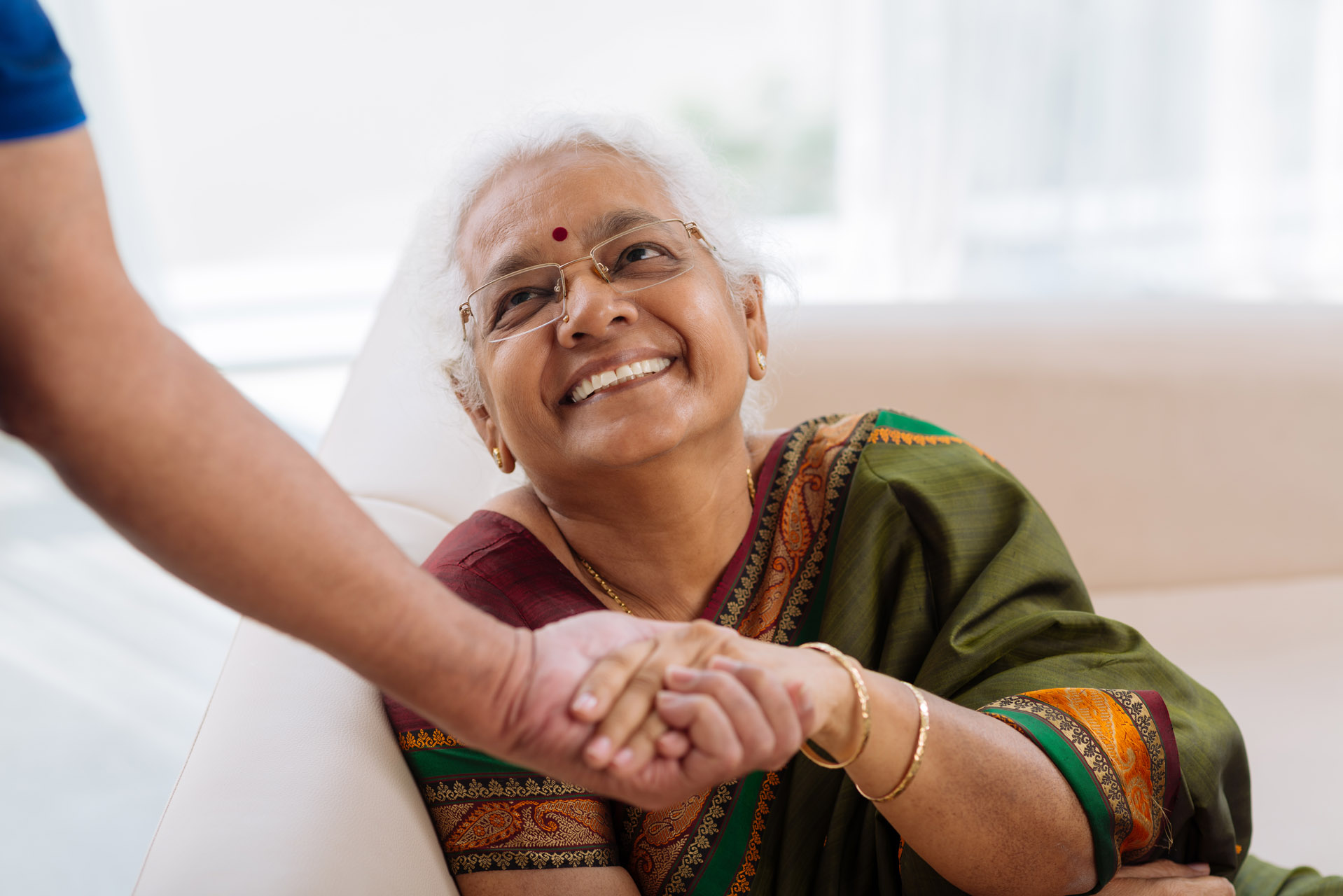 Indian lady sat at home holding the hand of her carer and smiling