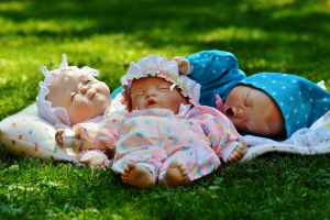 three dolls in frilly hats laying asleep on a cushion on the grass