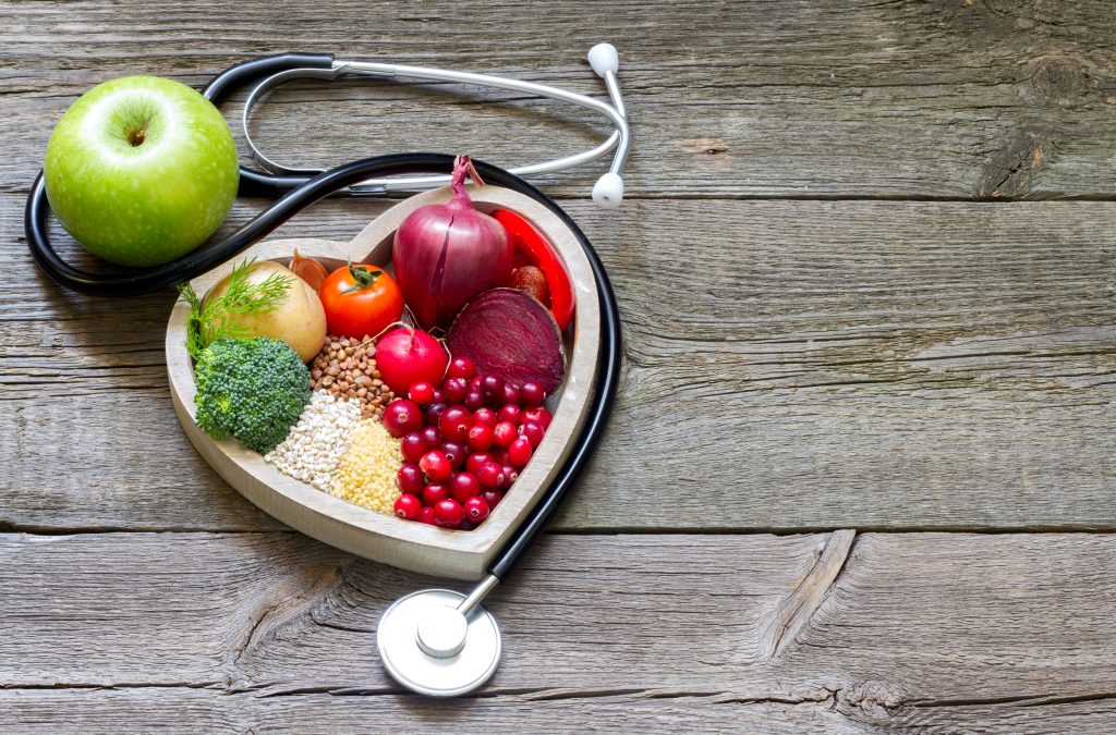Heart shape bowl full of vegetables and other foods to help you stay well in winter, with a stethoscope around it