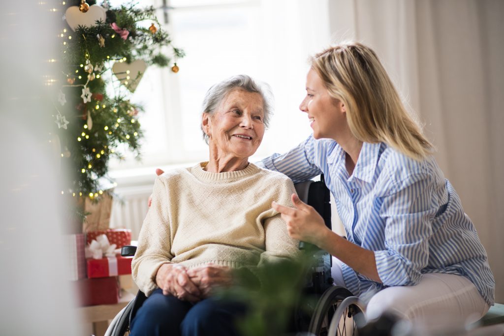 Lady crouched next to elderly lady in a wheelchair talking to her during Christmas visit