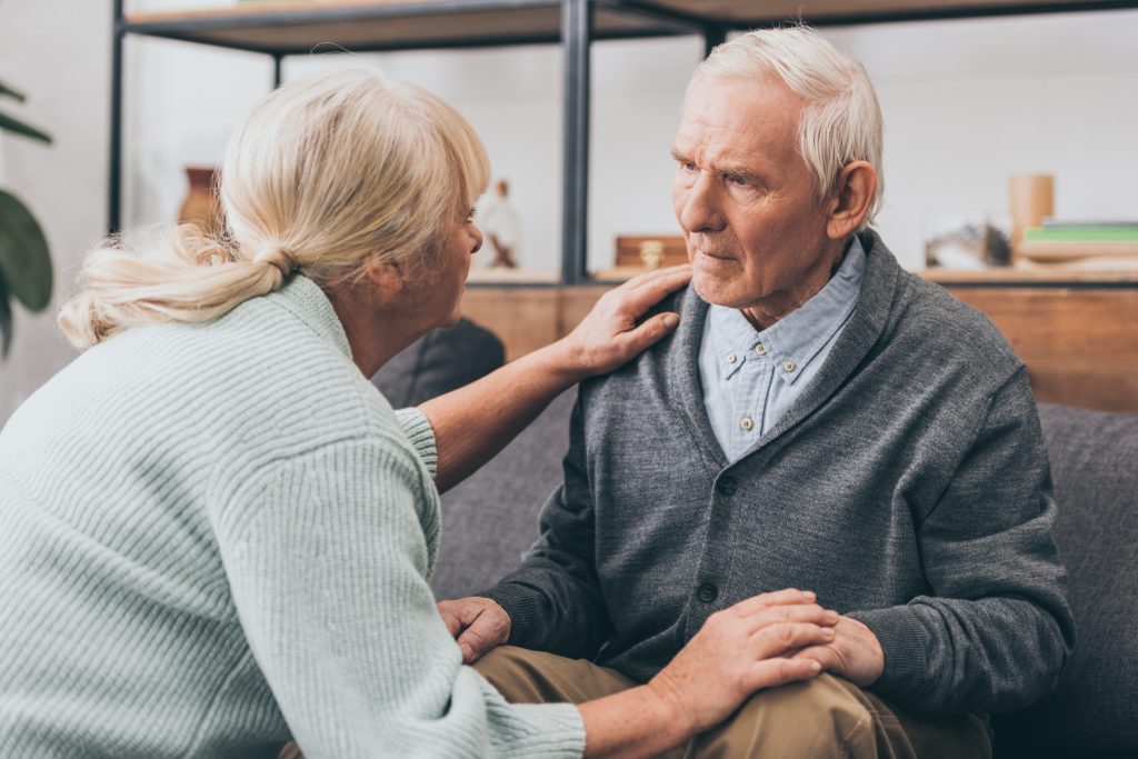 man with dementia sitting down, being comforted by wife