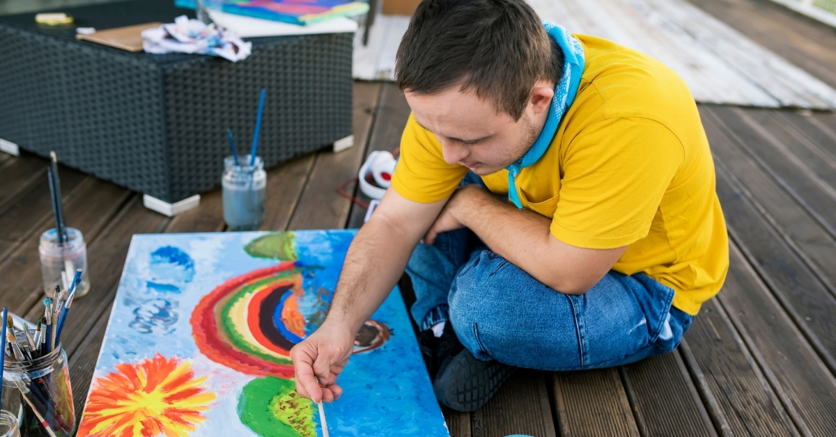 young man with learning disability painting a rainbow picture